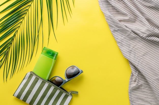 Zomer achtergrond. Samenstelling gestreepte cosmetische strandtas met sunblock en zonnebril op een gele achtergrond. Zomervakantie concept, zonnebrandcrème cosmetica en accessoires. Bovenaanzicht. Kopieer ruimte.