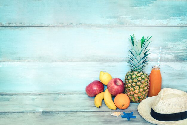 Foto zomer concept stillife. een stapel vers fruit, strohoed en een fles multivitamine sap voor een blauw rustiek hout.