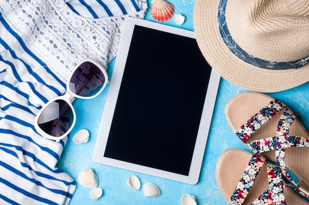 Foto zomer dames accessoires: zonnebril, hoed, sandalen, shirt en tablet op blauwe achtergrond