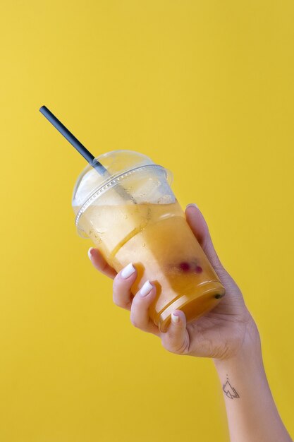 Zomer drankje verse limonade met sinaasappel in de plastic beker op gele achtergrond. vrouwelijke hand met een glas. Mockup voor uw advertentie. Ruimte kopiëren.