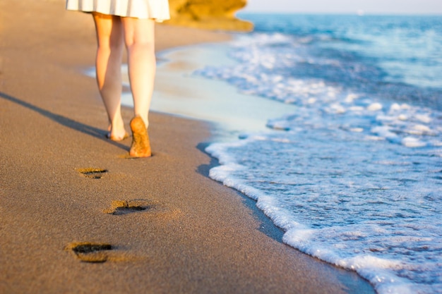 Zomer en reizen close-up van vrouwelijke benen en voetafdrukken op het zonsondergangstrand