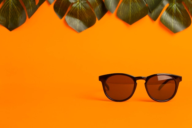 Zomer en vakantie concept. Zonnebril en tropische bladeren op een oranje achtergrond