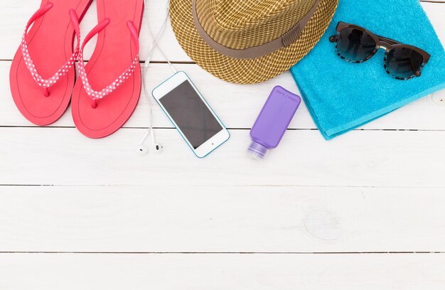 Zomer essentiële artikelen, waaronder flip-flops, hoed, handdoek en telefoon, gerangschikt op een wit houten oppervlak