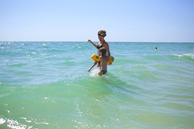 Zomer gelukkige familie van zes jaar blond kind spelen en springen watergolven omarmen vrouw moeder in zee kust strand