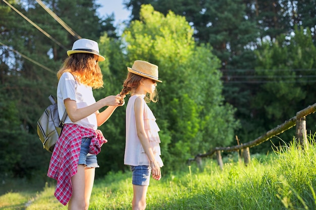 Zomer, gelukkige kinderen wandelen genietend van natuurvakantie, oudere zus vlecht haar jongere haar.