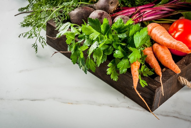 Zomer, herfstoogst. Verse biologische boerderij groenten in een houten kist op een witte marmeren tafel bieten, wortelen, peterselie, tomaten.