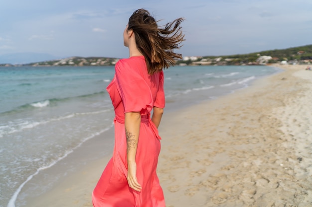 Zomer imago van gelukkig sexy vrouw in prachtige roze jurk die zich voordeed op het strand.