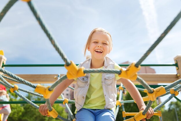 Zomer, jeugd, vrije tijd en mensen concept - gelukkig meisje op speelplaats voor kinderen klimrek