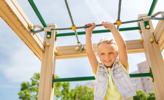 zomer, jeugd, vrije tijd en mensen concept - gelukkig meisje op speelplaats voor kinderen klimrek