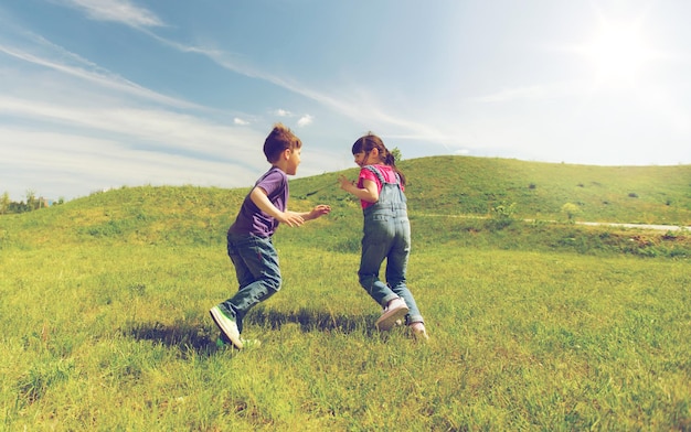 zomer, jeugd, vrije tijd en mensen concept - groep gelukkige kinderen die tag game spelen en buiten op groen veld rennen