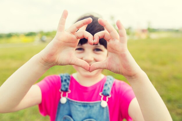 Foto zomer, jeugd, vrije tijd, liefde en mensenconcept - gelukkig meisje dat een hartvormig gebaar maakt op groen zomerveld