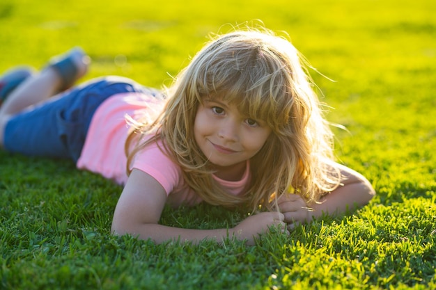 Zomer kind gezicht Glimlachend kind jongen met gras achtergrond Gelukkig jongetje liggend op het gras in het zomerpark Portret van een lachend kind liggend op groen gras buiten