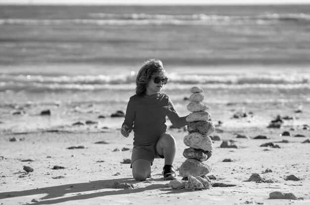 Foto zomer kind meditatie kind jongen met zen stenen op het strand meditatie spa en harmonie kalm evenwicht