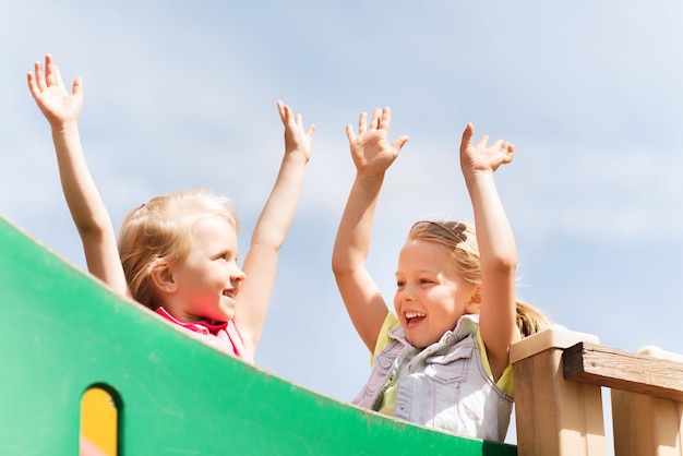 zomer, kindertijd, vrije tijd, vriendschap en mensenconcept - gelukkige kleine meisjes die handen zwaaien op kinderspeelplaats klimrek