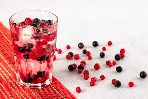 Zomer koud drankje met water, ijs en veelkleurige bessen op een rode keukenprop en witte tafel