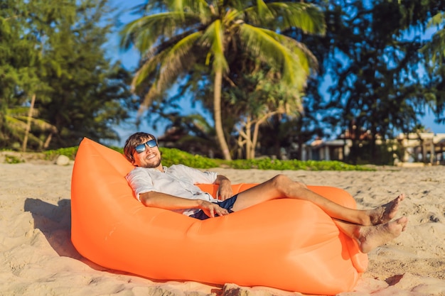 Zomer levensstijl portret van man zittend op de oranje opblaasbare bank op het strand van tropisch eiland ontspannen en genieten van het leven op luchtbed