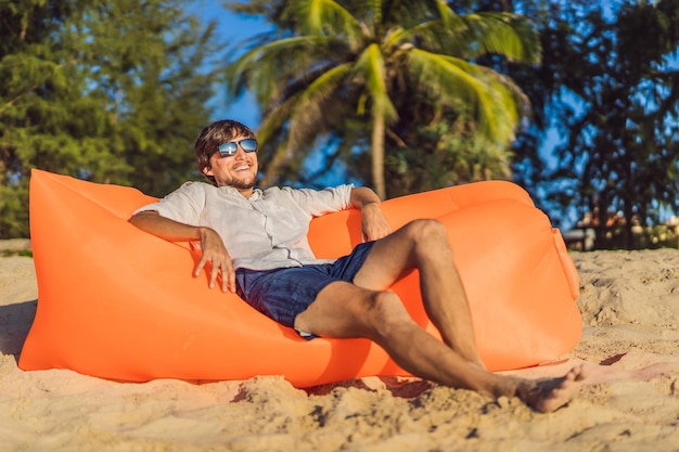 Zomer levensstijl portret van man zittend op de oranje opblaasbare bank op het strand van tropisch eiland ontspannen en genieten van het leven op luchtbed