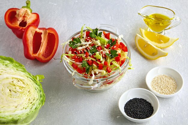 Zomer lichte salade van verse kool paprika en peterselie gekleed met olie sesamzaad en citroen in een glazen schaal omringd door ingrediënten op een lichte stenen tafel