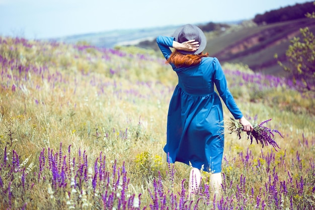 Zomer - mooi meisje op een weide met een boeket van wilde bloemen en traditioneel Oekraïens landschap