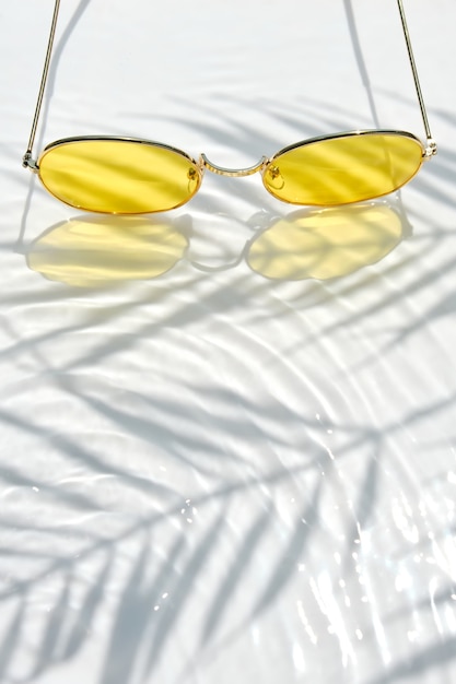 Zomer plat lag met gele zonnebril op water achtergrond met schaduwen van palmbladeren en kopieer ruimte. Concept van warme zomerdag op het strand.