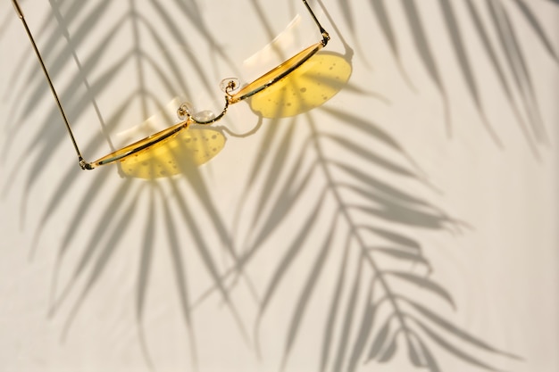 Zomer plat lag met gele zonnebril op water achtergrond met schaduwen van palmbladeren en kopieer ruimte. Concept van warme zomerdag op het strand.