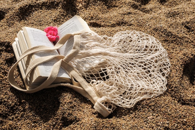 Zomer plat op een zandstrand Milieuvriendelijke boodschappentas van mesh en een boek