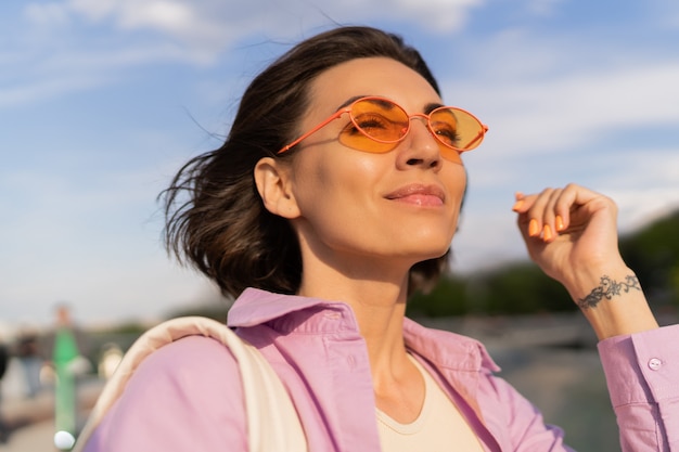 Zomer portret van vrij kortharige vrouw in stijlvolle zonnebril buiten wandelen