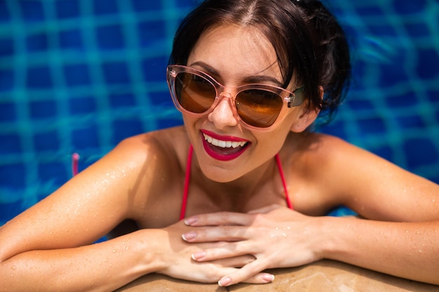 Zomer positieve portrsit van brunette vrouw in bikini die plezier heeft in het zwembad