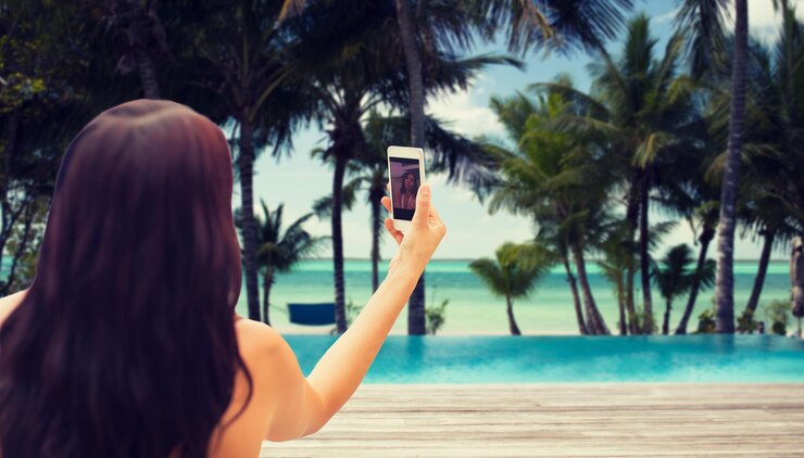 Foto zomer, reizen, technologie en mensenconcept - close-up van sexy jonge vrouw die selfie met smartphone neemt over tropisch strand met palmbomen en zwembadachtergrond