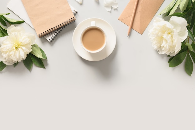 Zomer romantisch ontbijt met koffiekopje en witte pioenrozen bloemen op grijs bureau