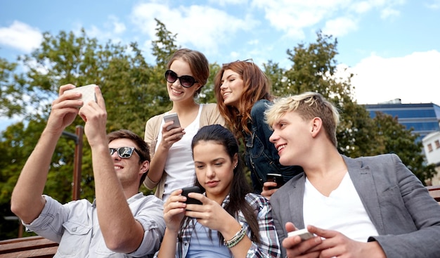 zomer, technologie, onderwijs en tienerconcept - groep gelukkige studenten of tieners met smarphones die selfie en sms-berichten op de campus nemen