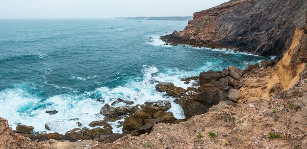 Zomer uitzicht op de Atlantische rotskust (Costa Vicentina, Algarve, Portugal). Grote steenachtige rockfall op afgrond kust en oceaan surfgolven.