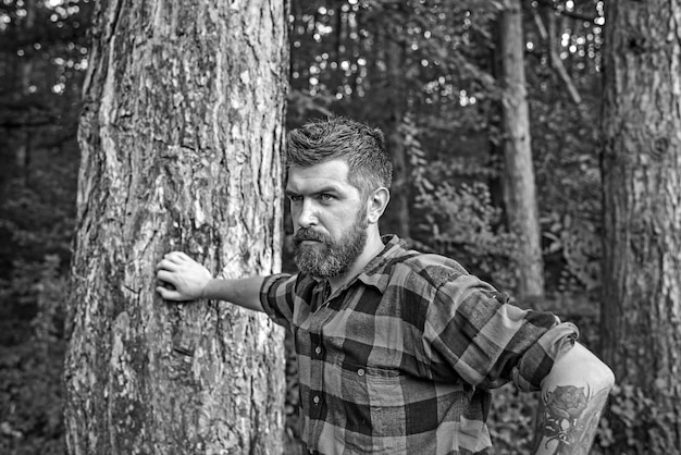 Zomer vakantie concept bebaarde man in bos Hipster met lange baard op natuurlijke groene landschap Toerist in geruite overhemd ontspannen bij boom reiziger wandelen op zonnige dag