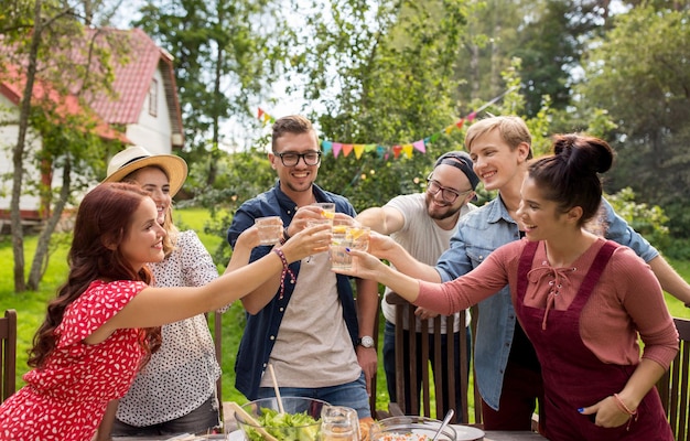 zomer, vakantie, feestmensen en voedselconcept - gelukkige vrienden hebben een tuinfeest en rammelende glazen