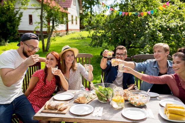 zomer, vakantie, feestmensen en voedselconcept - gelukkige vrienden hebben een tuinfeest en rammelende glazen