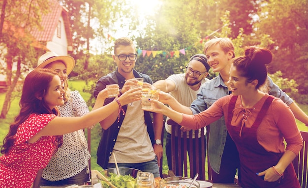 zomer, vakantie, feestmensen en voedselconcept - gelukkige vrienden met tuinfeest en rammelende glazen