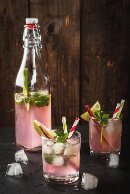 Zomer verfrissend drankje, cocktail. Zelfgemaakte organische mojito of limonade met rabarber, munt en limoen. Op een zwarte betonnen stenen tafel, in glazen en een fles. Kopieer ruimte