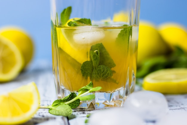 Zomer verfrissend drankje in een glas. Traditionele koude zoetzure limonade met citroen, munt en ijsblokjes op een grijze houten tafel.