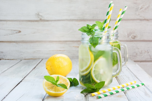 Zomer verfrissende detox cocktail. Water met citroen, munt en ijs in glazen pot op witte houten bord. Rustieke stijl.