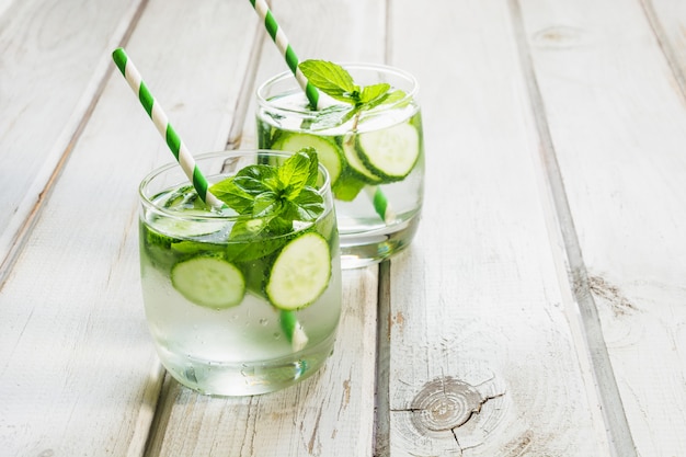 Zomer verfrissende detox cocktail. Water met komkommer, munt en ijs in glas op witte houten plank.