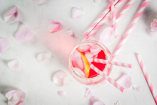 Zomer verfrissing drankjes. Lichtroze rozencocktail, met rose wijn, theeblaadjes, citroen. Op een witte stenen betonnen tafel. Met gestreepte roze buisjes, bloemblaadjes en roze bloemen. bovenaanzicht