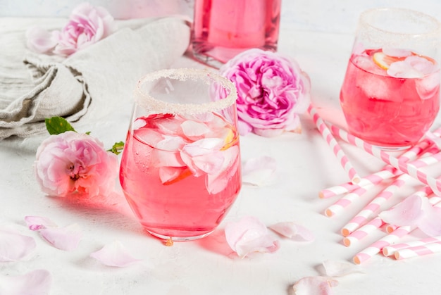 Foto zomer verfrissing drankjes. lichtroze rozencocktail, met rose wijn, theeblaadjes, citroen. op een witte stenen betonnen tafel. met gestreepte roze buisjes, bloemblaadjes en roze bloemen.