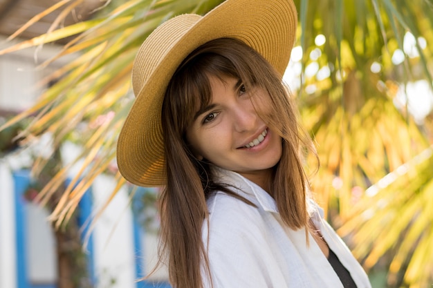 Zomer vportrait van vrij brunette vrouw in strooien hoed poseren buiten.