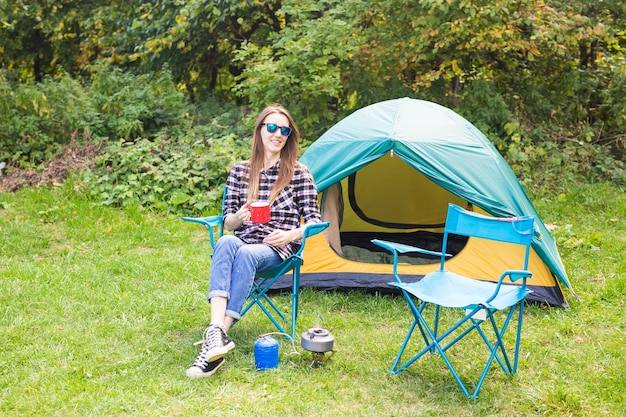 Zomer, wandeling, toerisme en natuur concept - jonge vrouw zit in de buurt van tent.