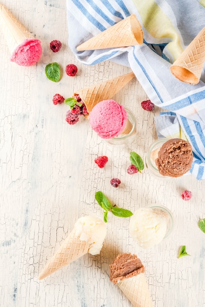 Zomer zoete bessen en desserts, verschillende ijssmaak in kegels roze (framboos), vanille en chocolade met munt op licht beton