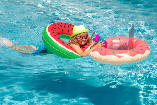 Zomerbedrijf en online technologiekind dat op laptop werkt vanuit het zwembad