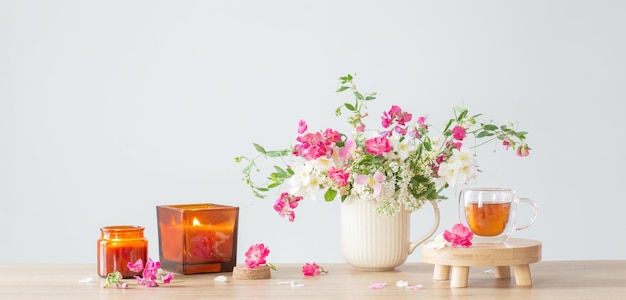 Zomerbloemen brandende kaarsen en kopje thee op lichte achtergrond