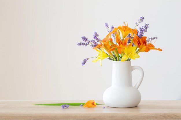 Zomerbloemen in witte kan op houten plank