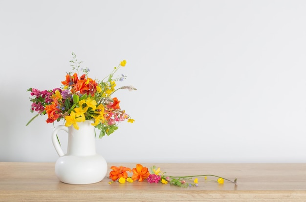 Zomerbloemen in witte kruik op houten tafel