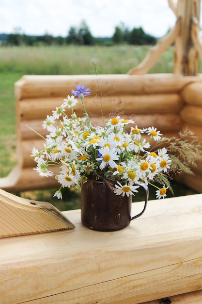 Zomerboeket van margrieten, in een ijzeren vaas, op een houten ondergrond, wilde bloemen